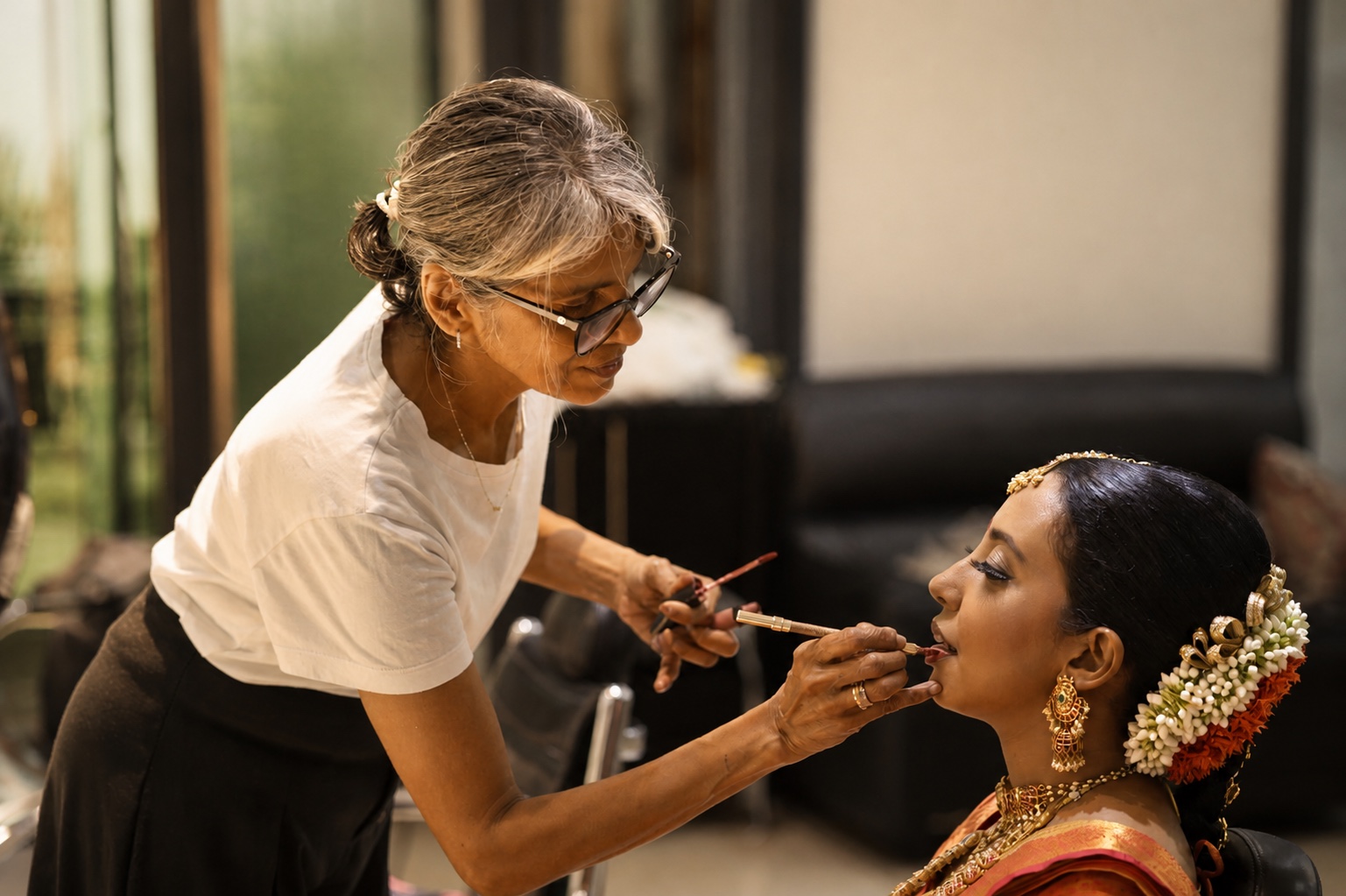 A Salon Nayana artist applying lipstick to a bride in traditional jewellery and jasmine flowers
